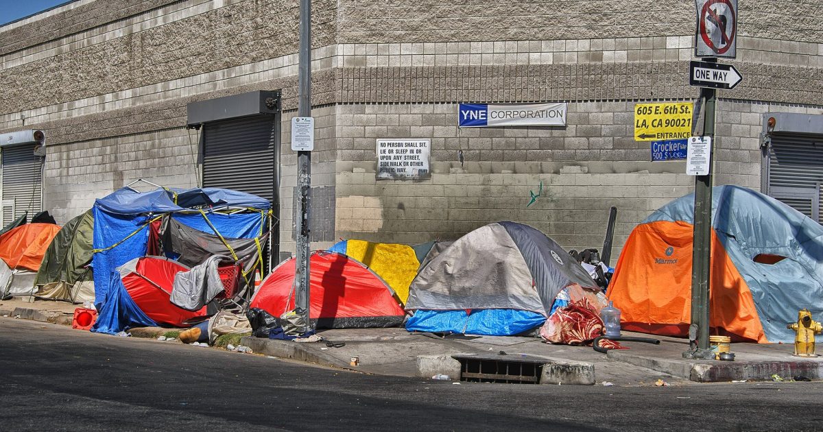 Colorful tents line a city sidewalk, highlighting homelessness and urban challenges in a metropolitan area.