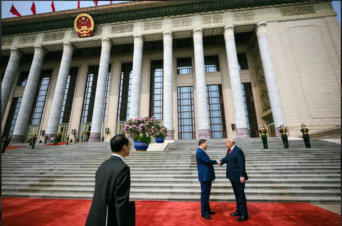 Chinese President Xi Jinping shakes hands with a foreign leader on the steps of the Great Hall of the People, surrounded by security and floral arrangements.