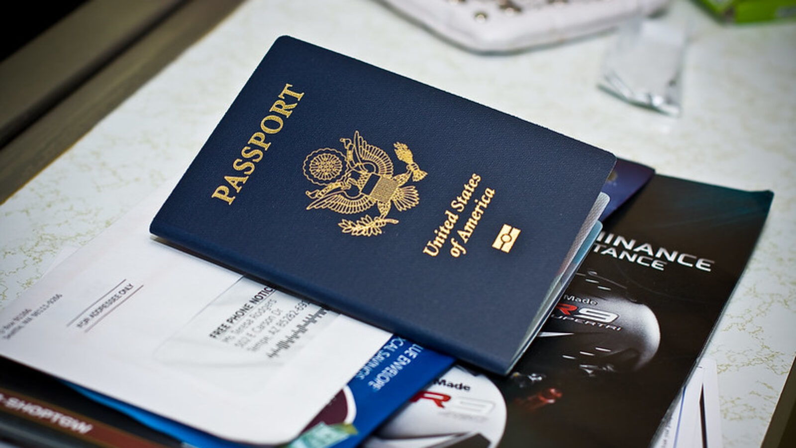 United States passport resting on top of various documents and brochures on a table.