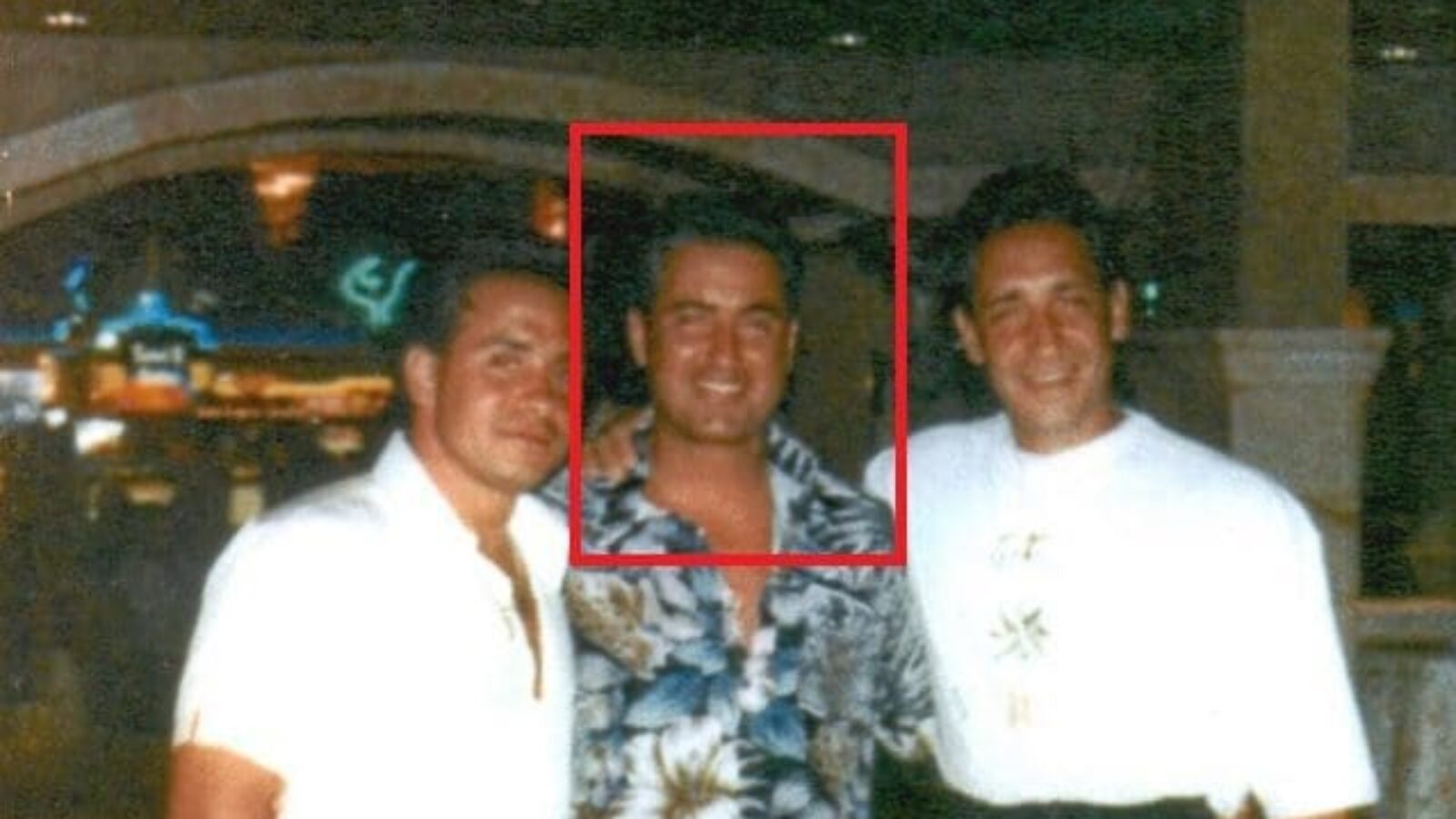 Three men posing together in a casino, with one wearing a colorful floral shirt, capturing a nostalgic moment in a lively atmosphere.