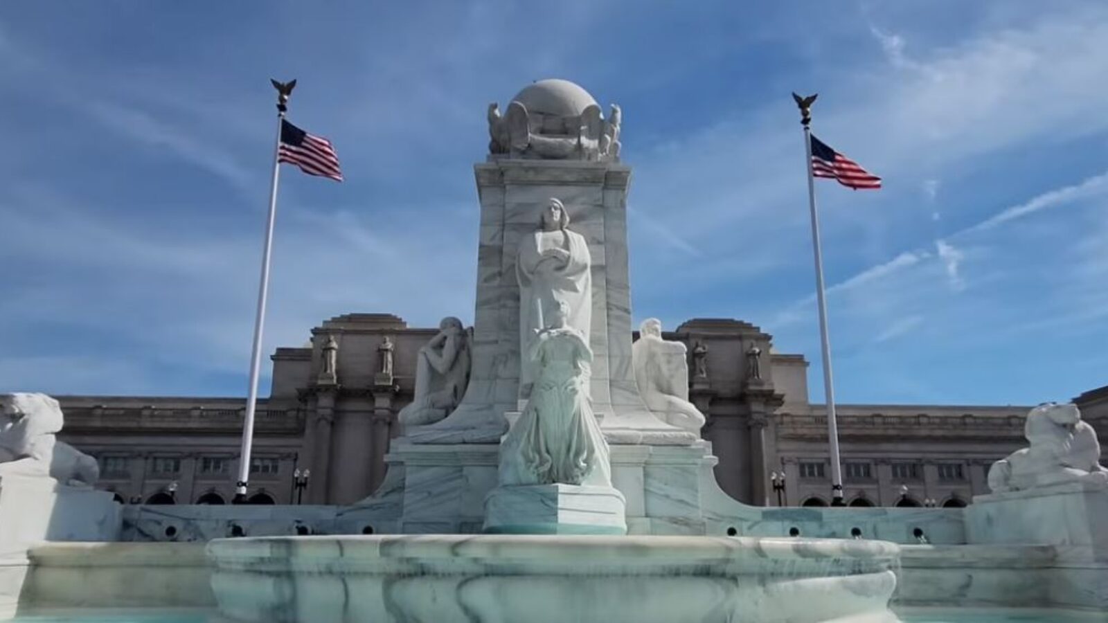 Historic marble monument featuring statues and American flags against a blue sky, located in a prominent public space.