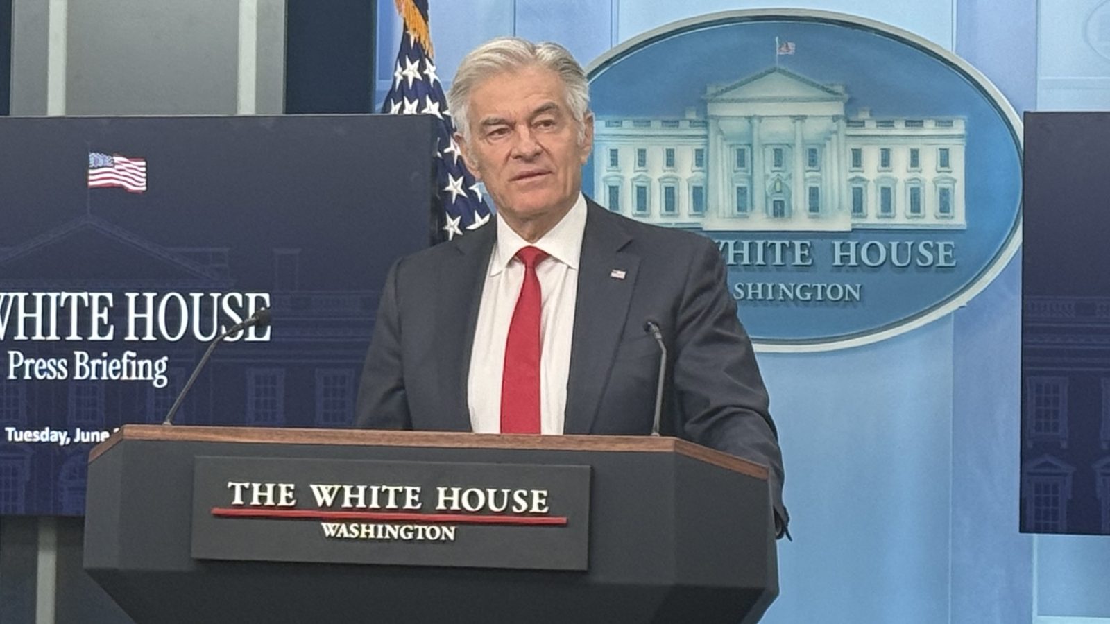 White House press briefing with a speaker in a suit and red tie, discussing important national issues in front of the iconic White House backdrop.