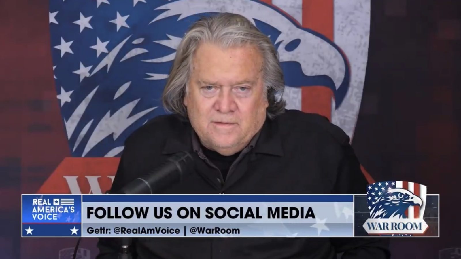 Steve Bannon speaking on the War Room podcast, with a backdrop featuring American flags and a prominent eagle logo.