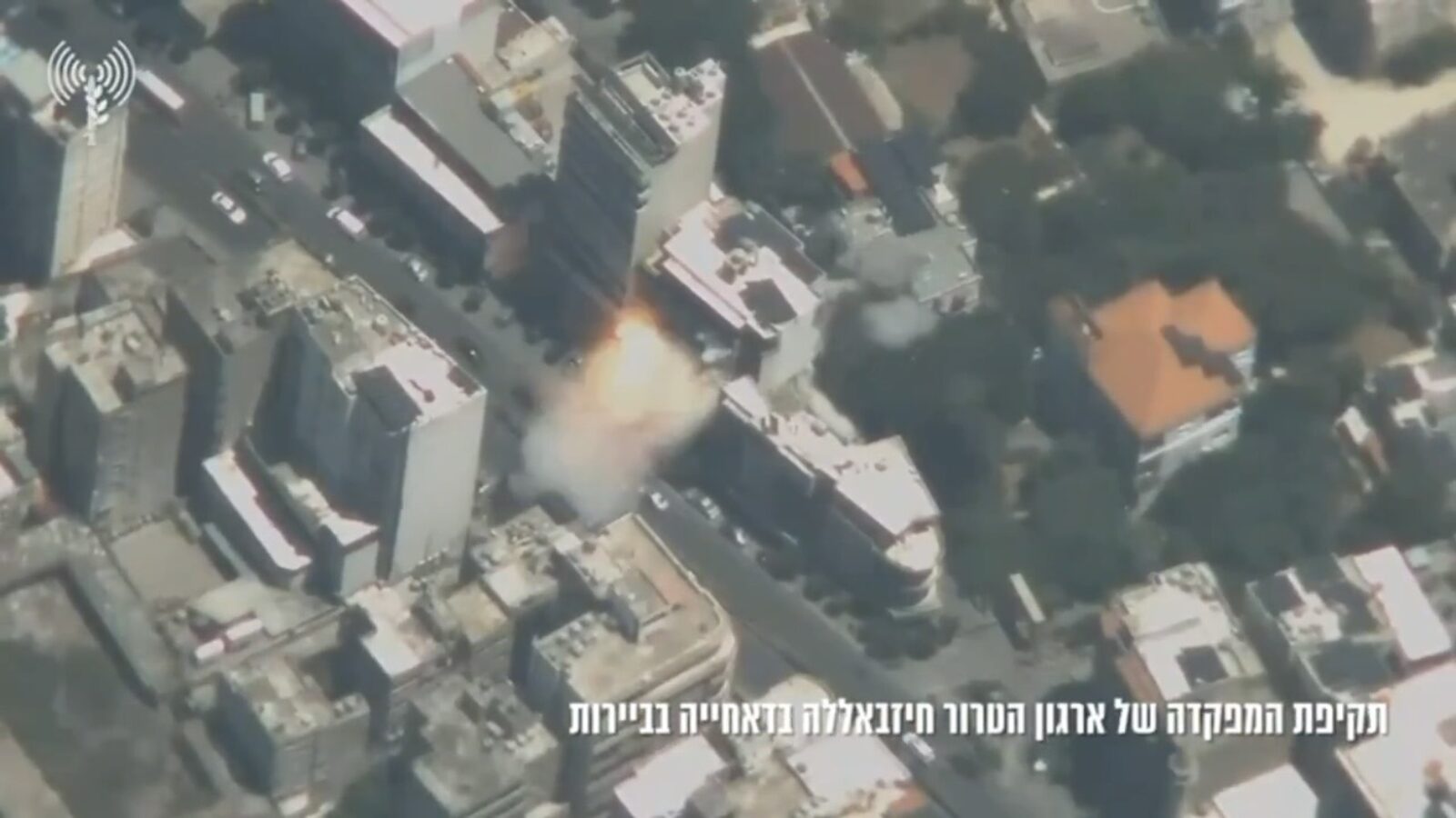 Aerial view of a building explosion in an urban area, with smoke and debris rising from the site.