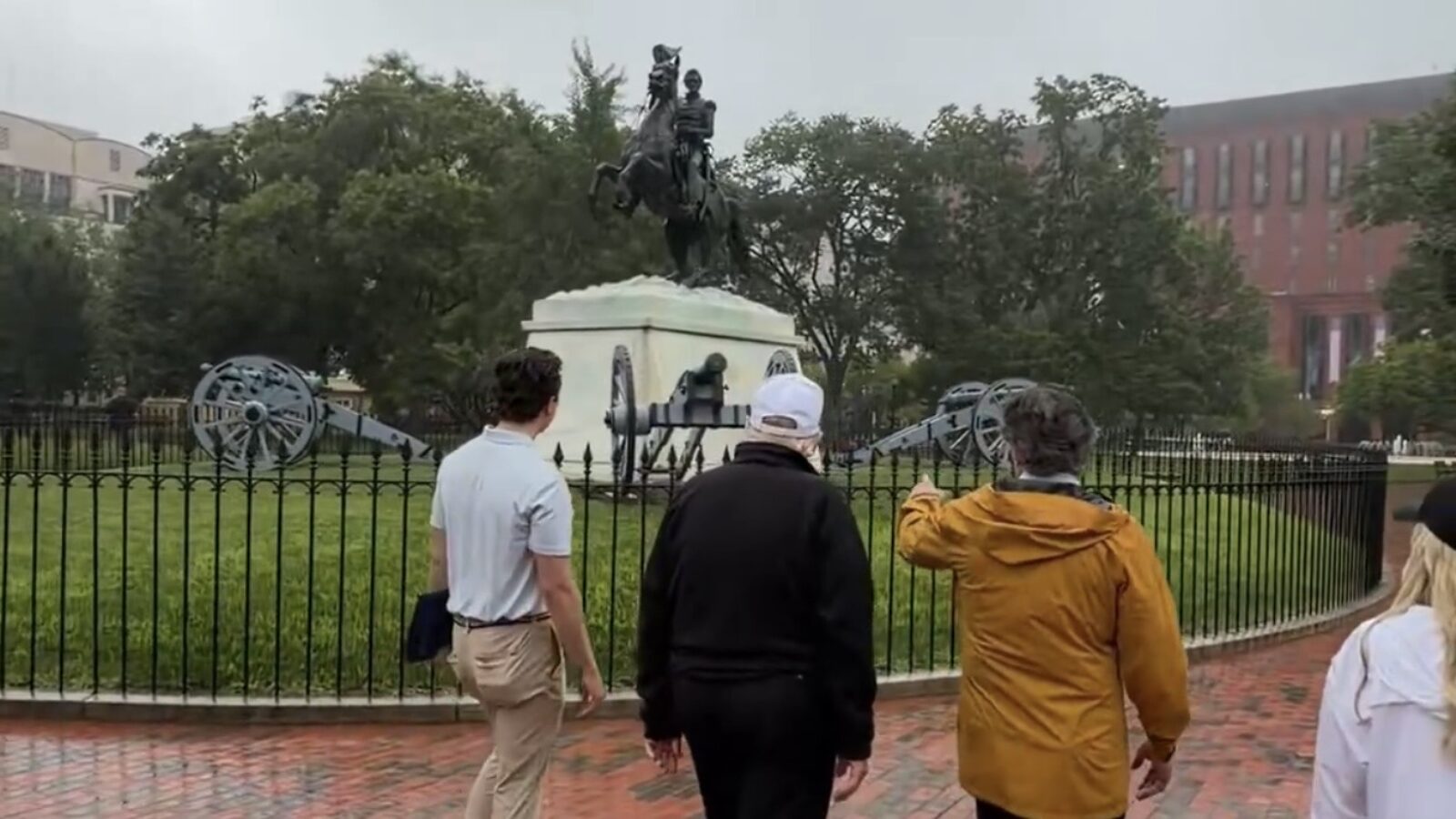 Visitors admire a historical statue and cannons in a foggy park setting, showcasing a moment of exploration and reflection.
