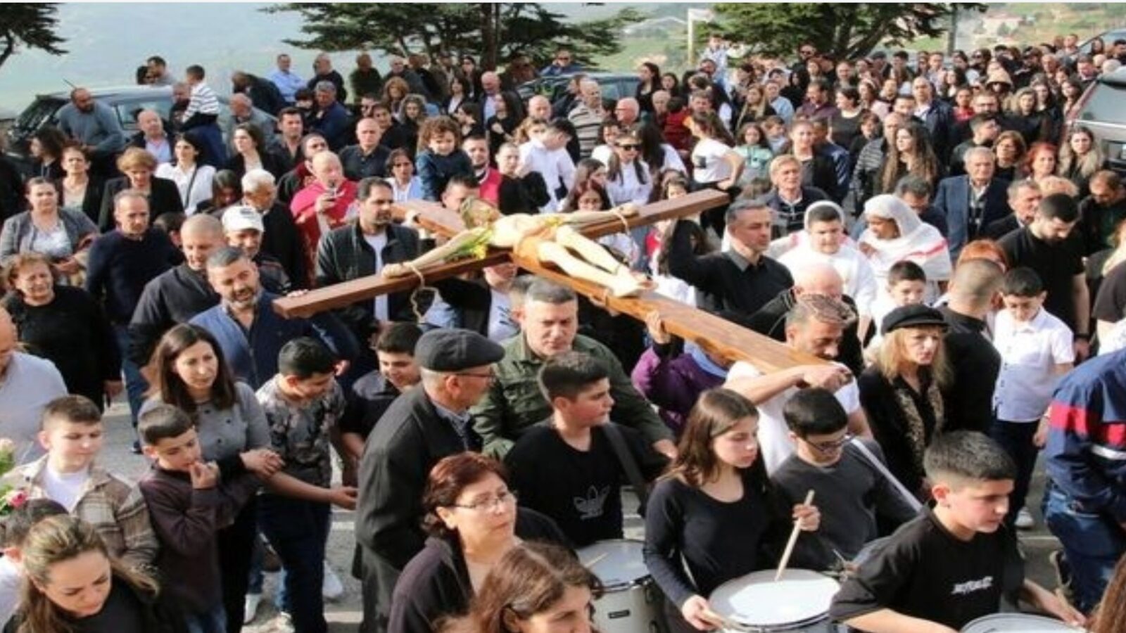 Crowd participating in a religious procession, carrying a large wooden cross, showcasing a vibrant community gathering.