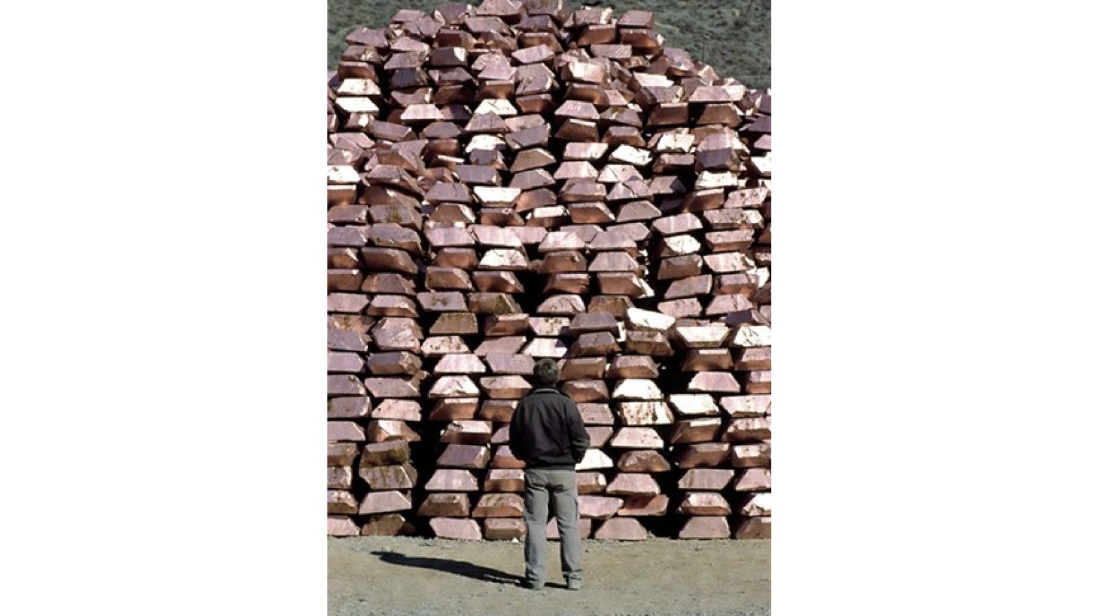 Man observing a large pile of copper ingots in an industrial setting, highlighting the scale of metal production and storage.