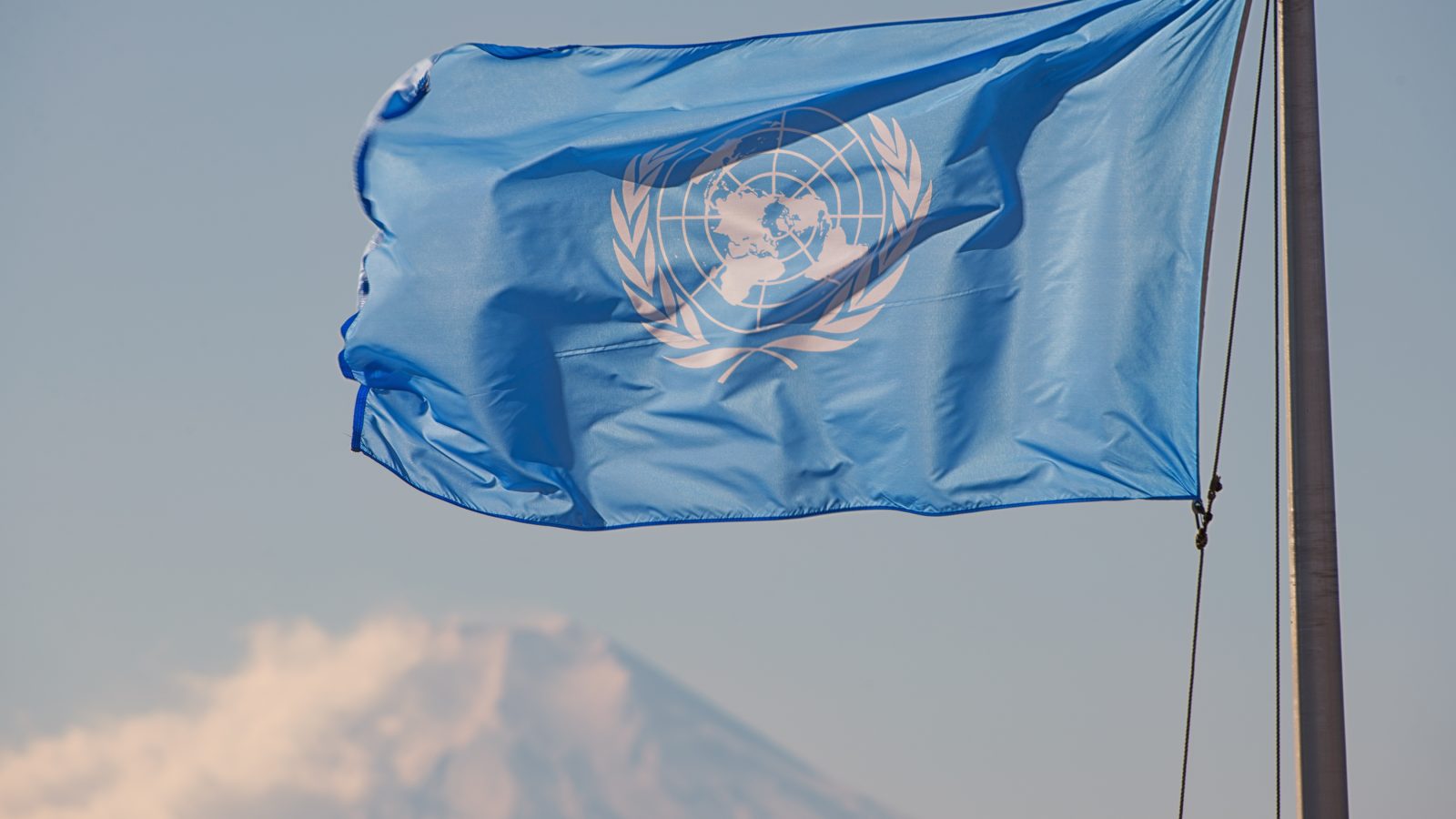 United Nations flag waving in front of a mountain, symbolizing global cooperation and peace initiatives.