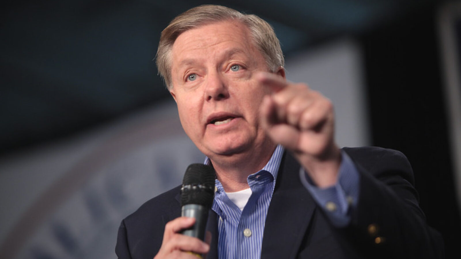 Lindsey Graham speaking passionately into a microphone at a political event, gesturing with his hand to emphasize his points.