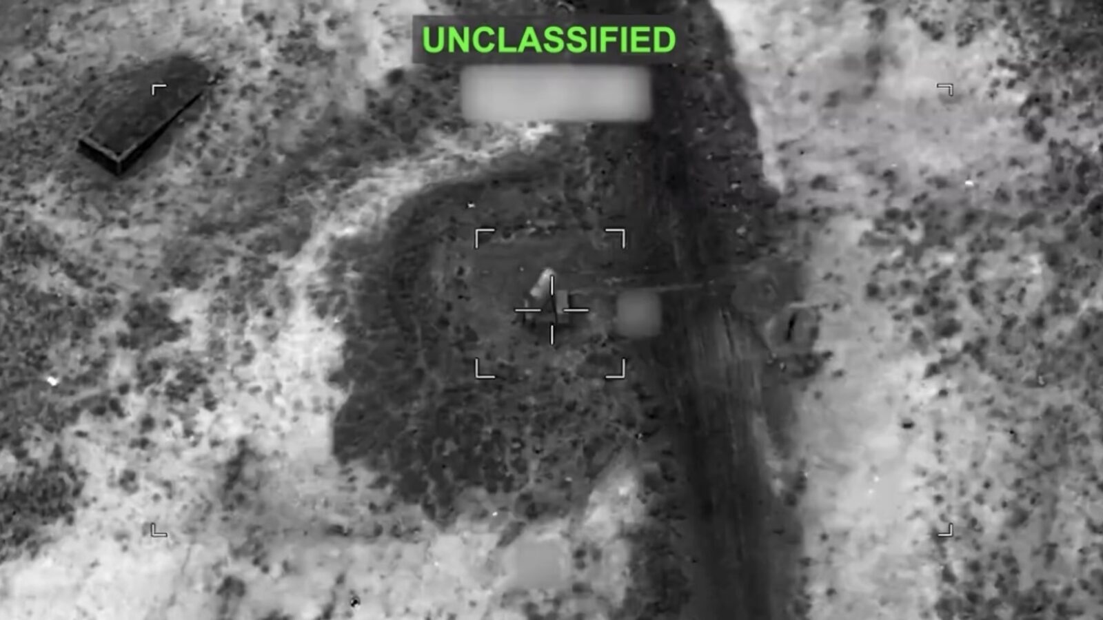 Aerial view of an unclassified area showing a targeted object in a desert landscape with surrounding vegetation and terrain features.