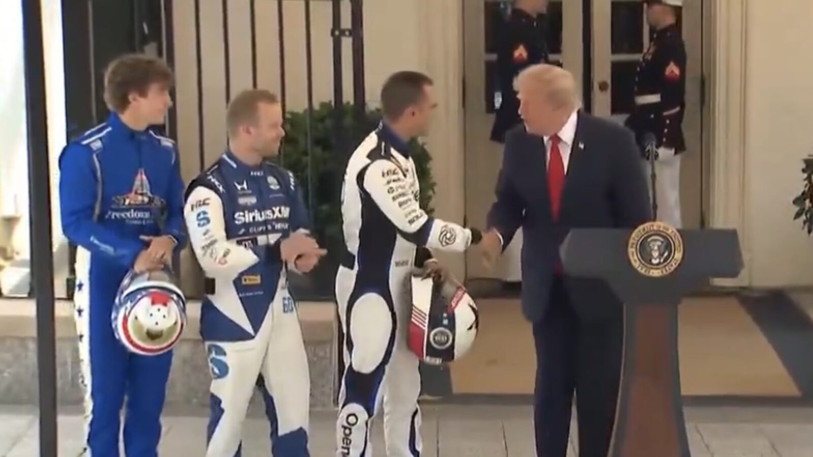 Donald Trump shakes hands with race car drivers at a ceremony, showcasing a celebration of motorsports at the White House.