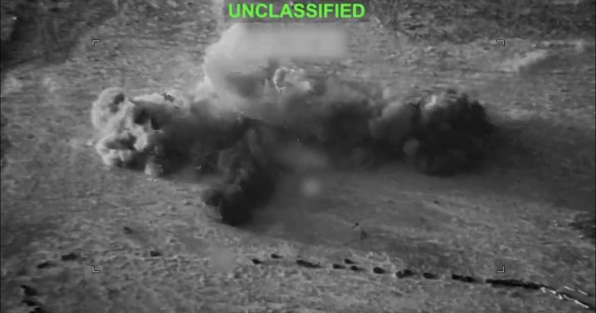 Aerial view of a large explosion producing smoke and debris in a military context, labeled as unclassified.