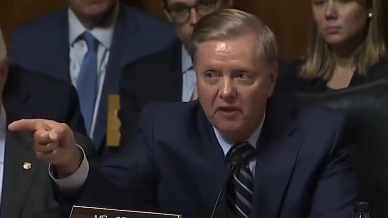 Lindsey Graham gestures while speaking during a Senate committee hearing, with other committee members visible in the background.