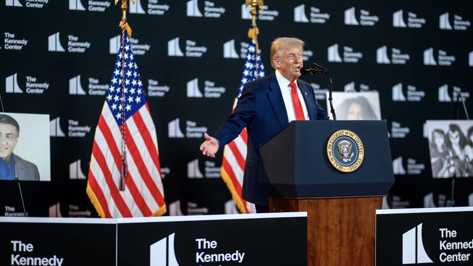 Former President Donald Trump speaking at a podium during an event at the Kennedy Center, with American flags and portraits in the background.
