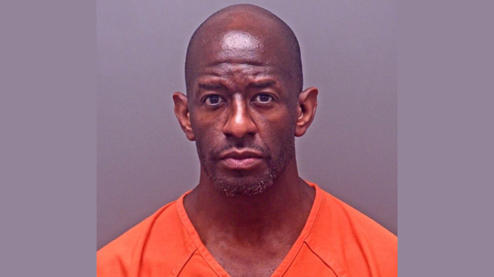 Mugshot of a man in an orange prison jumpsuit, looking directly at the camera with a serious expression.