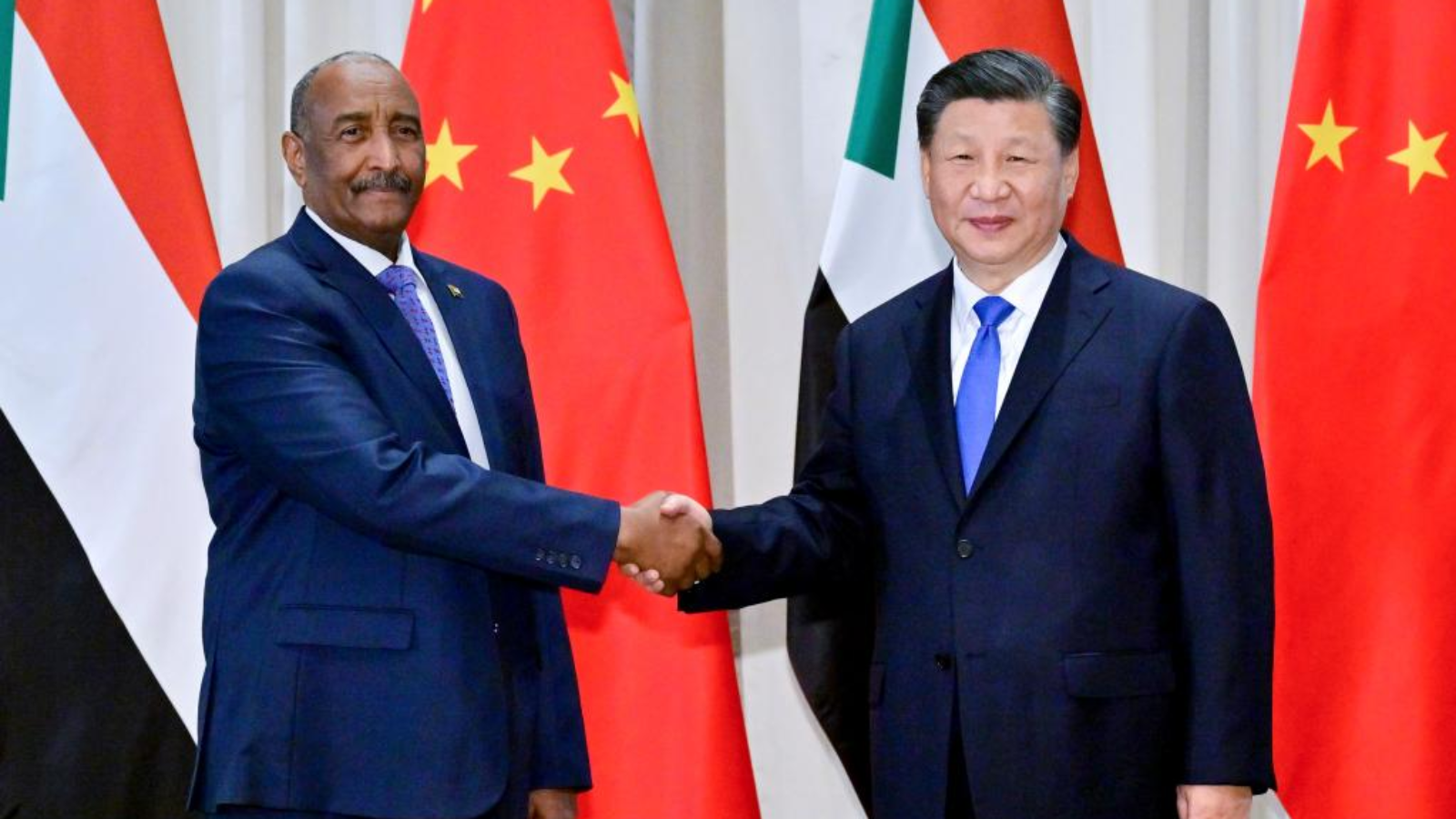 Sudanese leader and Chinese President Xi Jinping shake hands during a diplomatic meeting, surrounded by flags of Sudan and China.